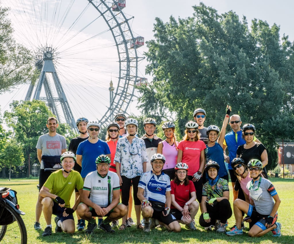 Gruppo di ciclisti in posa di fronte alla Ruota Panoramica di Vienna, Austria.